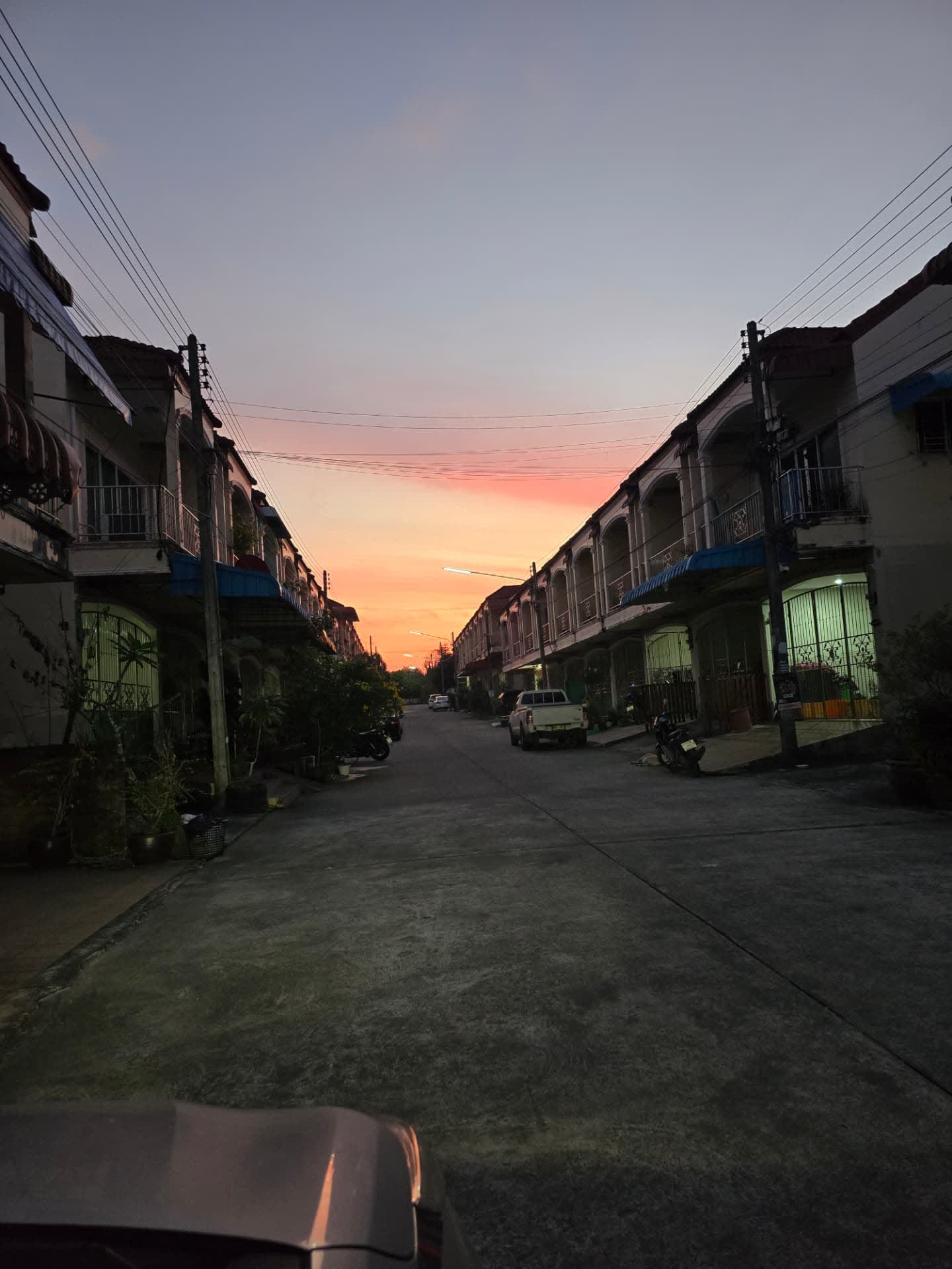 ถนนในหมู่บ้านย่านหาดใหญ่ช่วงพระอาทิตย์ตก มีบ้านทาวน์เฮาส์และรถจอดอยู่สองข้างทาง